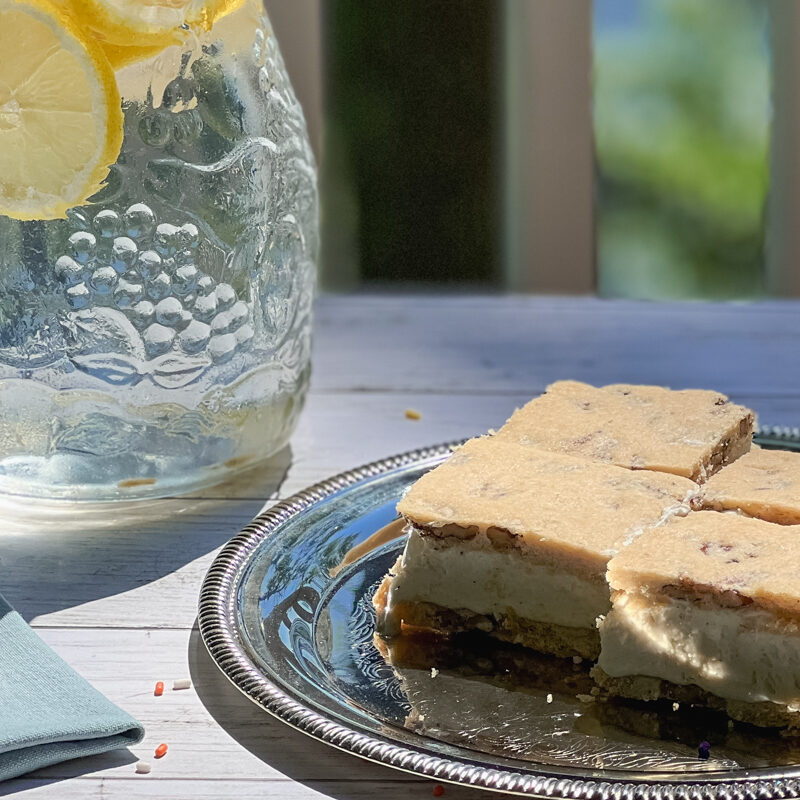 Butter Pecan Maple Ice Cream Sandwiches on a platter, napkin, and in a jar of sprinkles with a pitcher of lemonade nearby.