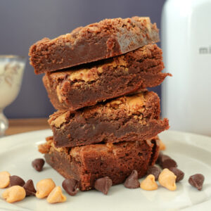 Brownies stacked on a white plate with chocolate and butterscotch chips scattered around.