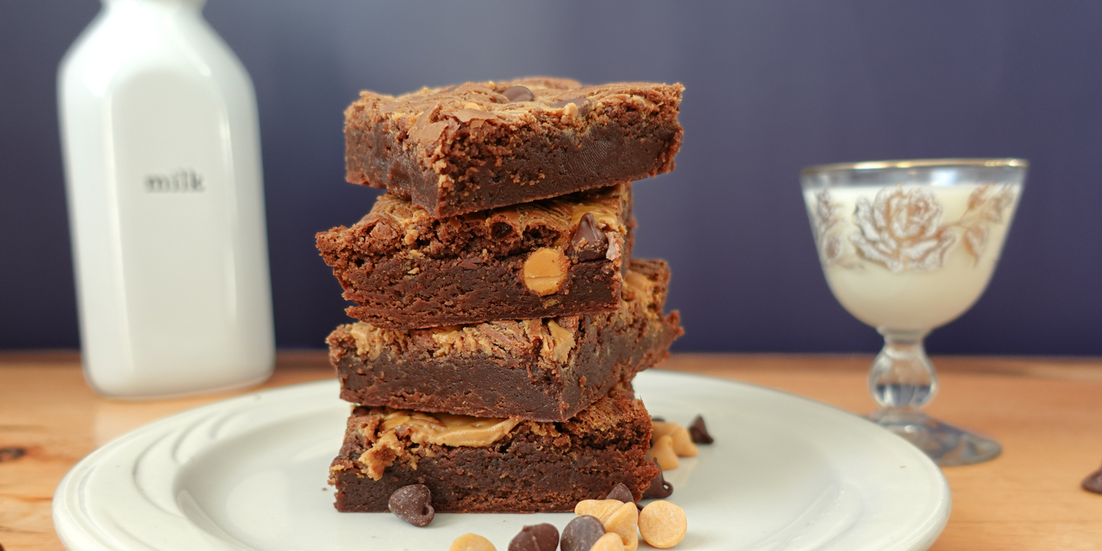 Chocolate Fudge Peanut Butter Brownies stacked on a white plate with milk in the background.