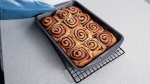 Cinnamon rolls fresh baked in their baking tray on a cooling rack.