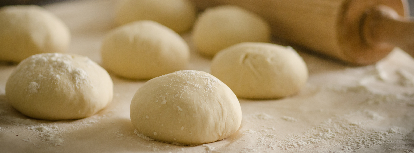 Pie dough ready to be rolled out with a rolling pin in the distance.
