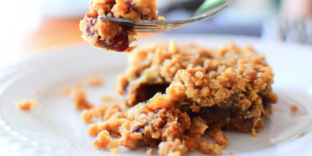 Date square on a plate with a piece of it on a fork suspended in the air.