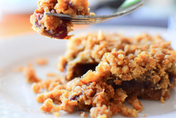 Date square on a plate with a piece of it on a fork suspended in the air.