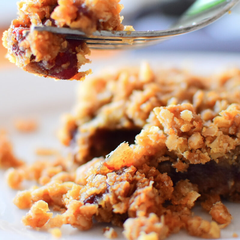 Date square on a plate with a piece of it on a fork suspended in the air.