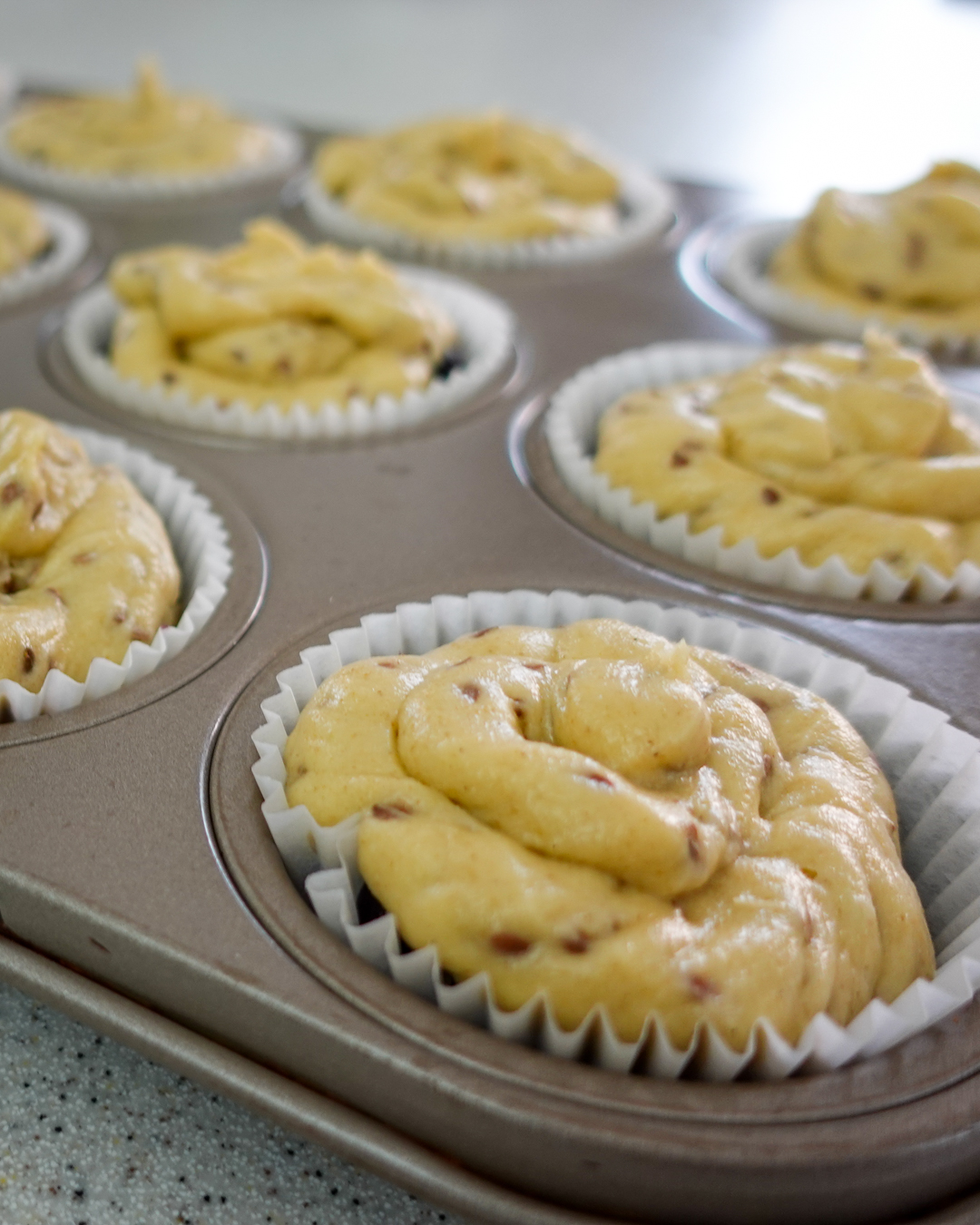 Pictured is a muffin pan with muffin liners and piped batter in each cup.