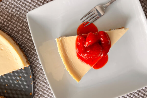 A slice of cheesecake on a white plate with strawberry syrup.