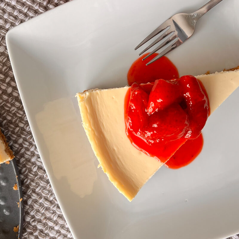 A slice of cheesecake on a white plate with strawberry syrup.