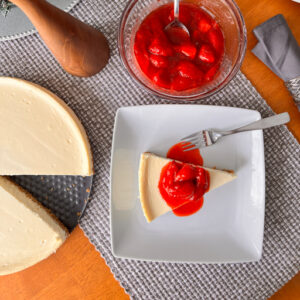 Homemade cheesecake on a white plate with strawberry topping.