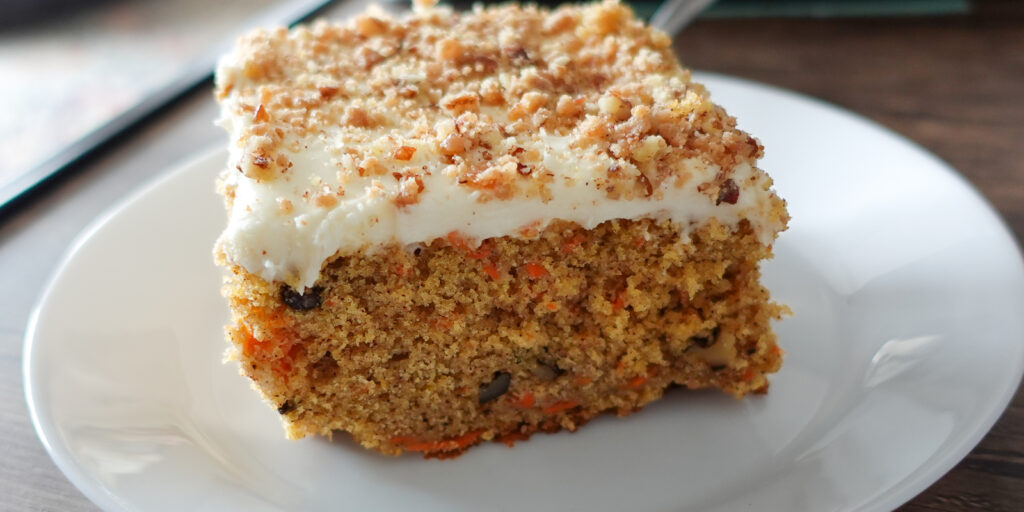 This image shows a slice of carrot cake on a white plate to highlight the best recipe for moist carrot cake.