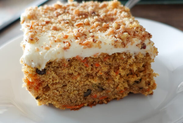 This image shows a slice of carrot cake on a white plate to highlight the best recipe for moist carrot cake.