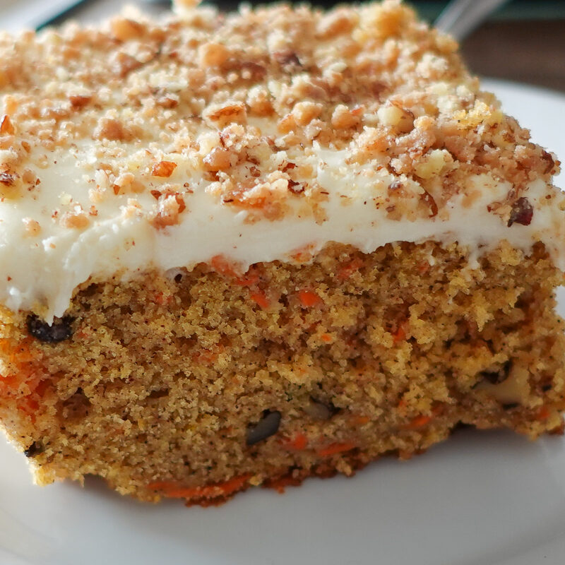 This image shows a slice of carrot cake on a white plate to highlight the best recipe for moist carrot cake.