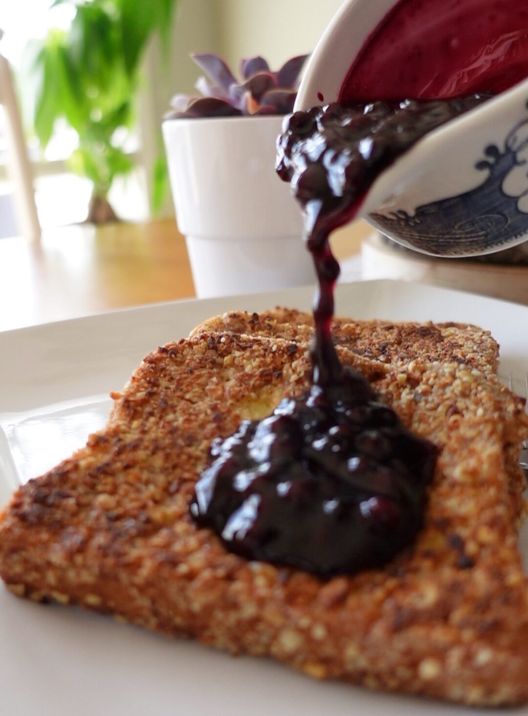 This is an up close image of blueberry sauce being drizzled over granola crusted french toast.