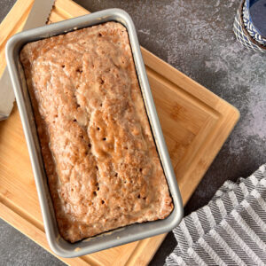 This is an image of zucchini bread in a 9x5 pan on a wooden cutting board.