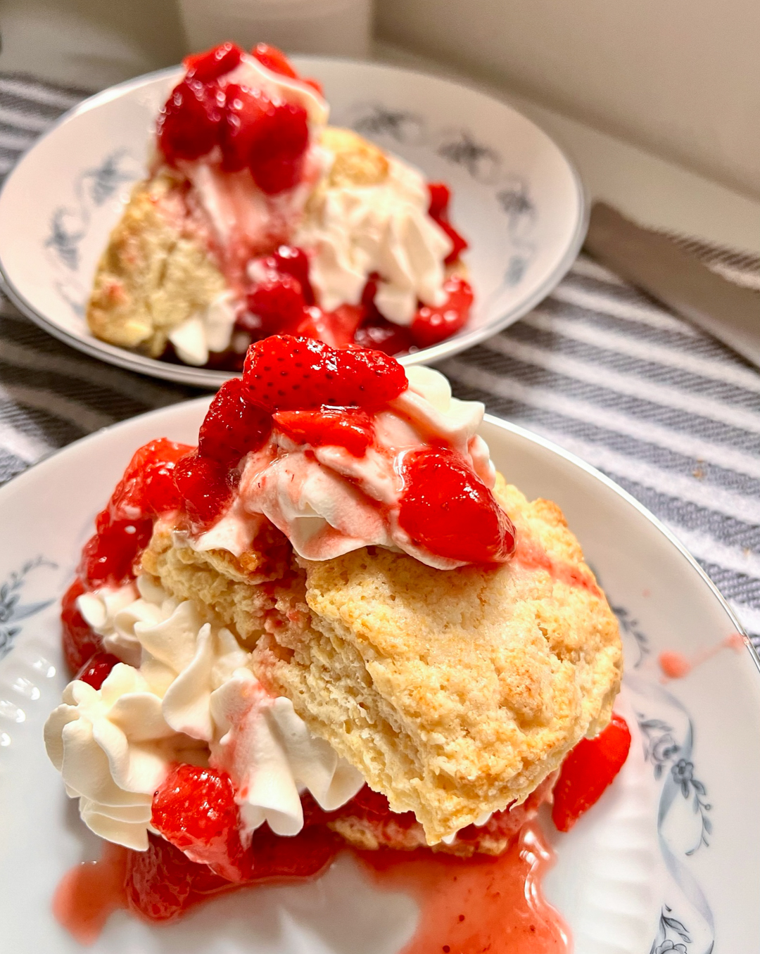 This is an image of strawberry shortcake on a white plate with a second portion in the distance.