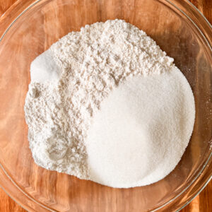 Flour, sugar, baking powder, and salt in a large clear glass bowl.