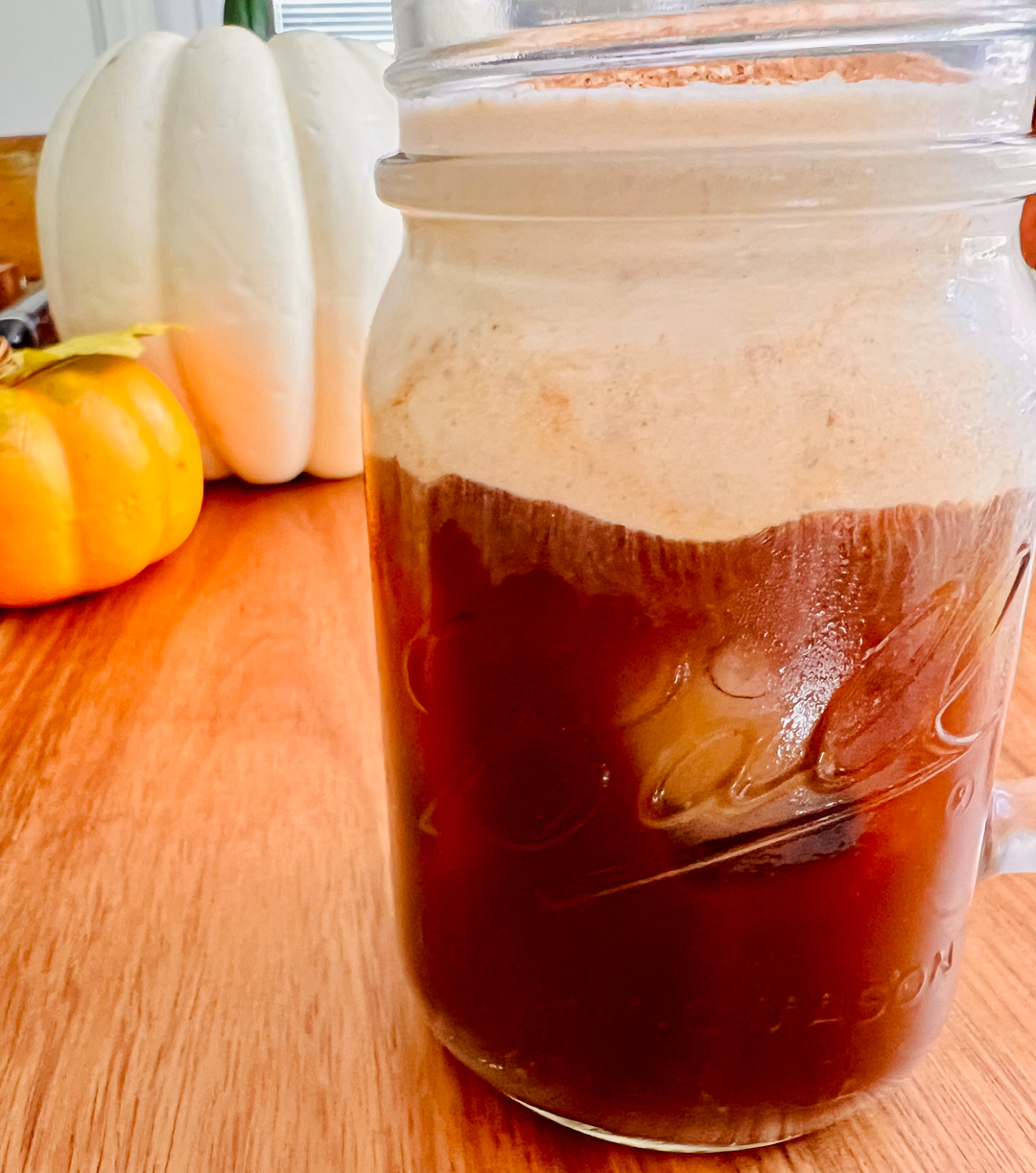 This is a side view of a mason jar filled with cold brew and topped with pumpkin cold foam.