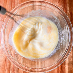 An image of melted butter, milk, eggs, and vanilla extract being whisked together.