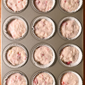 An image of a muffin tray with muffin liners filled with batter 2/3 of the way full.