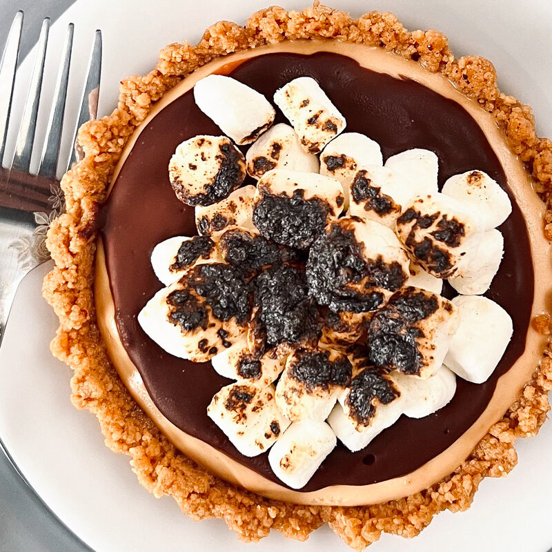 This is a top-down view of a peanut butter s'mores tart, which is on a white plate.