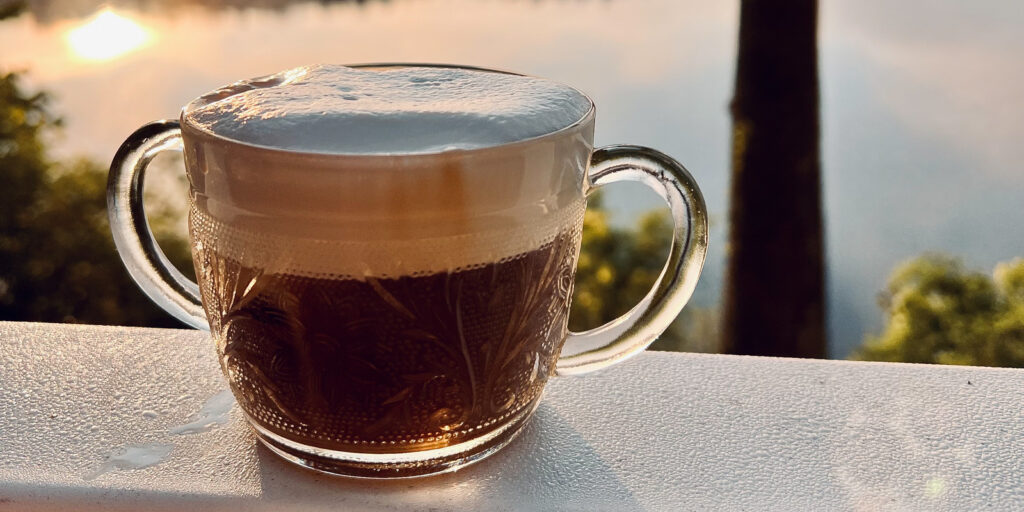 An image of cold brew in a cup on a white railing overlooking a water scene.