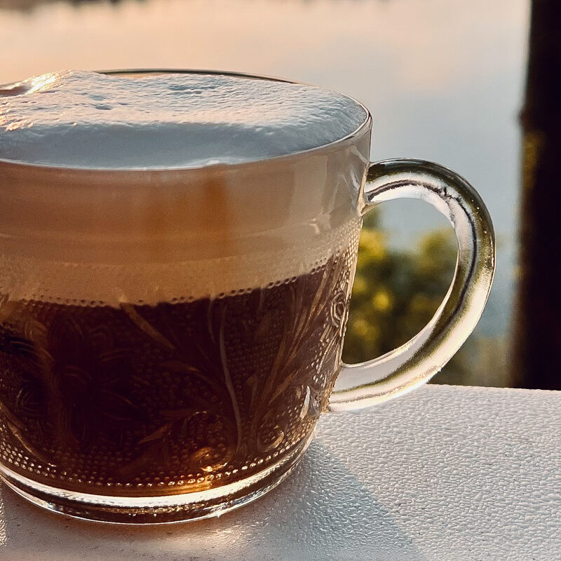 An image of cold brew in a cup on a white railing overlooking a water scene.