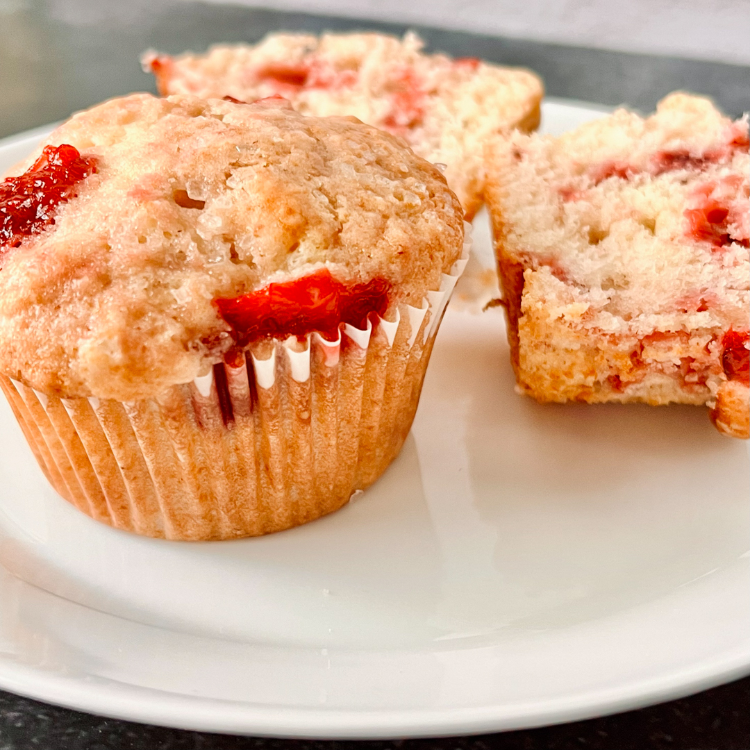 Two muffins on a white plate with one split open.