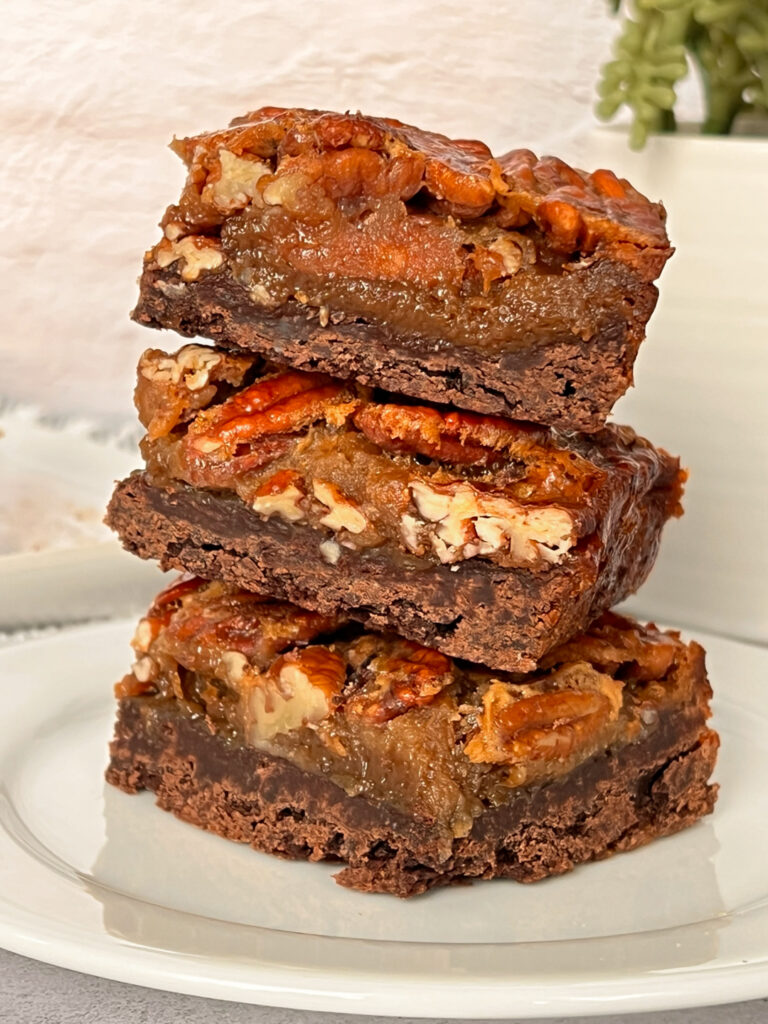 Three pecan pie bars atop a white plate with against a light backdrop.