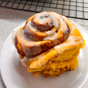 A pumpkin spice latte cinnamon roll on a white plate.