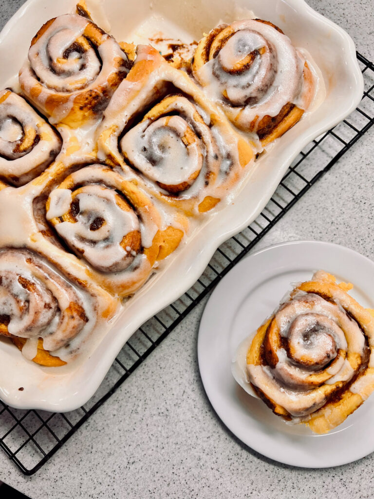 Overhead image of pumpkin rolls, one on a white dish and the rest in their white baking pan.